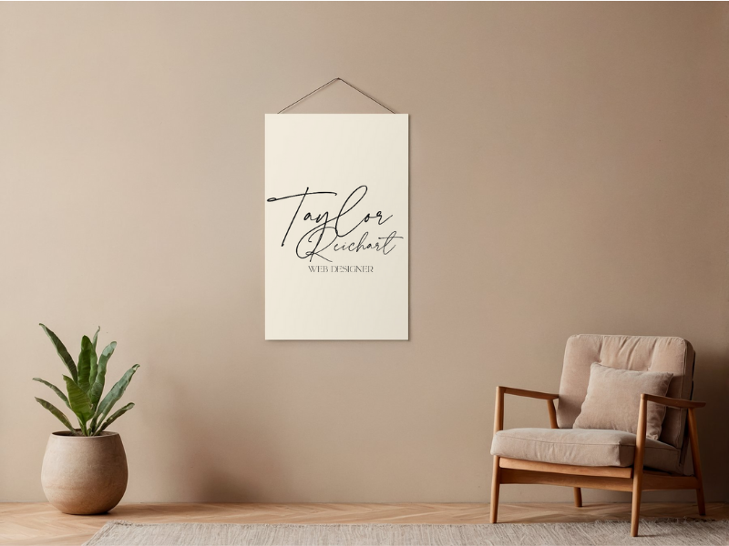Simple, minimalist office setup with a green plant and chair, featuring a wall sign that says “Taylor Reichart, Web Designer,” reflecting a modern web designer workspace aesthetic.